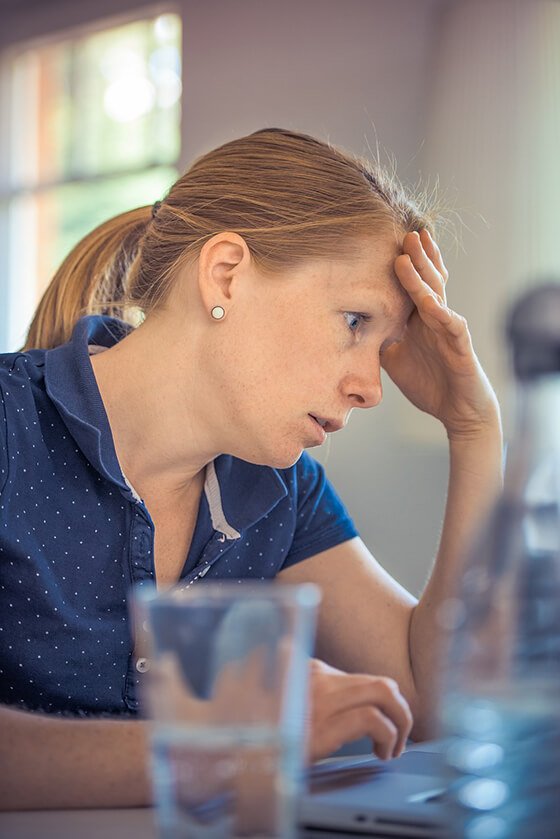 imagem de mulher com o braço apoiado sobre uma mesa e a mão sobre a testa representando insatisfação e preocupação